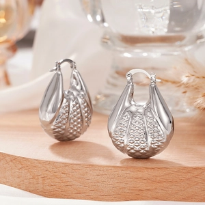 Détail de boucles d'oreilles argentées style coquillage avec texture tressée sur bois