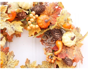 Close-up of autumn wreath with pumpkins, maple leaves and pine cones on white door