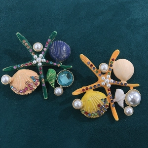 Close-up of colorful enamel starfish and seashell brooches with pearls on green velvet