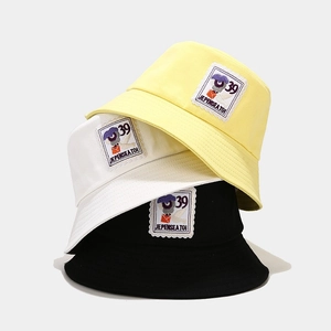 Close-up of three cotton bucket hats in yellow, white, and black with embroidery detail