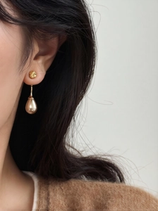Detail close-up of vintage golden drop pearl earrings worn with a brown knit sweater