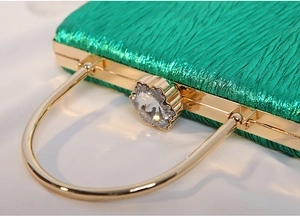 Detail of emerald pleated clutch bag featuring crystal flower clasp and gold handle