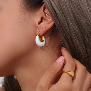 Close-up of white resin and gold metal C-shaped hoop earrings on model with a ring