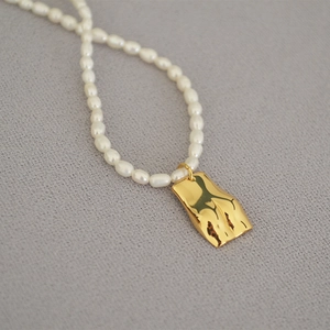 Detail of freshwater rice pearls and a vintage golden torso pendant on a grey fabric background