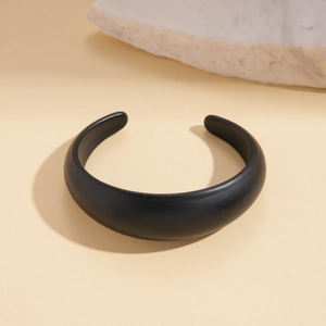 Detail of matte black irregular geometric open bangle against minimalist stone background