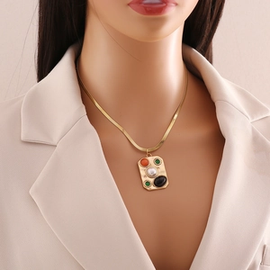 Close-up of gold snake chain necklace with rectangle pendant inlaying pearl and gemstones