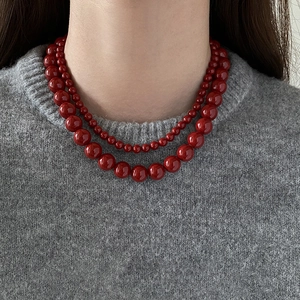 Gros plan d'un collier à double rang de perles rouges sur un pull gris chic