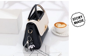 Detail of contrast handbag with metal arc handle and minimalist black bear charm
