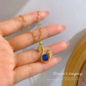 Macro view of gold swan pendant necklace featuring micro-set stones and a blue core