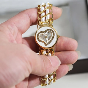 Detailed macro of a women's gold quartz watch with woven strap and diamond heart dial