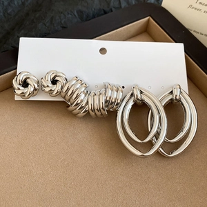 Detail view of silver oval C-shaped earrings and braided studs on a jewelry display tray