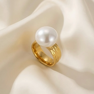 Detailed close-up of a large white pearl on a gold textured ring over silk fabric