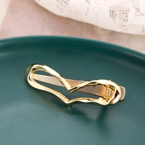 Golden wavy heart-shaped metal hair clip on a green ceramic plate with lace