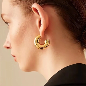 Close-up of polished gold C-shape hoop earrings worn by model with minimalist metal texture