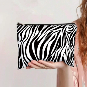 Detail of zebra print canvas makeup bag held by a model with a gold zipper closure