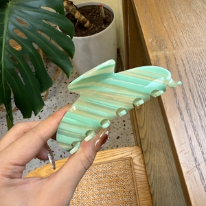 Detail of mint green marble acetate hair claw clip held in hand for size display