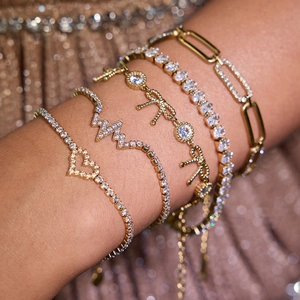 Close-up of stacked gold stainless steel bracelets with zirconia heart and crown charms