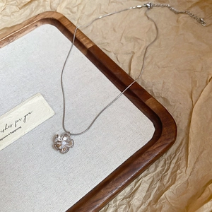 Detailed macro view of silver flower pendant with pearl on a wooden jewelry display tray