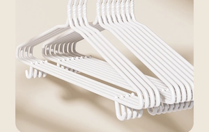 Close-up of white non-slip hangers stacked diagonally against a warm beige background