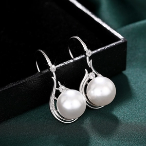 Close-up of elegant white pearl drop earrings with sparkling zircon on black velvet