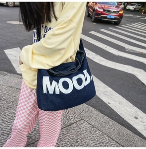 Outdoor street style shot of large denim tote bag with MOOD print and yellow hoodie