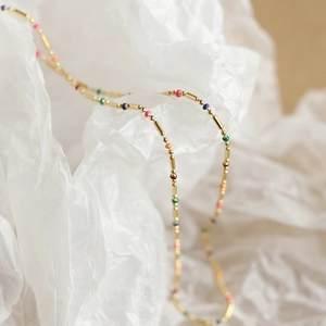 Detail of 18K gold plated titanium necklace with colorful enamel beads on white paper