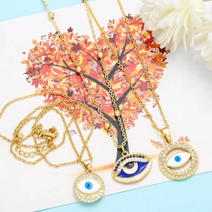Detailed close-up of three 18K gold-plated evil eye pendants with sparkling blue enamel and crystals