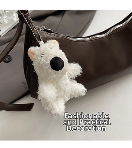 Close-up of fluffy white bear charm with metal chain on dark brown faux leather bag