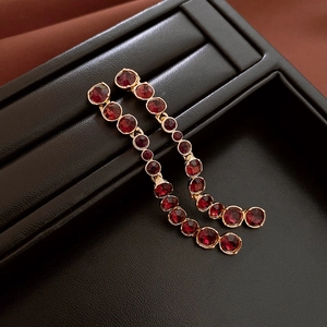 Detail of red rhinestone tassel earrings with gold-toned finish on black leather display