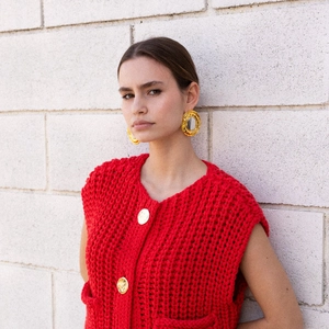 Close-up of model wearing large gold-tone round geometric earrings with red knit vest