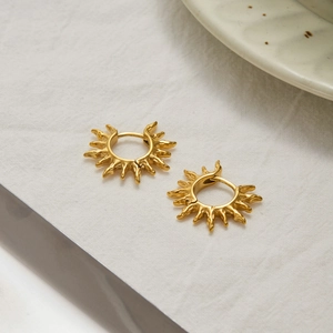 Detail shot of 18K gold plated stainless steel sunburst hoop earrings on textured surface