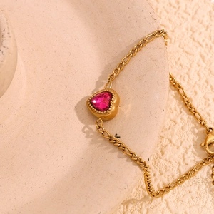Macro view of a 18K gold-plated Figaro chain bracelet with a pink heart zircon stone