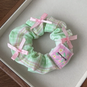 Close-up of handmade plaid scrunchie with pink silk bows and floral tag detail