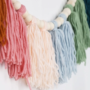 Detailed close-up of handmade colorful yarn tassels and natural wooden beads wall decor