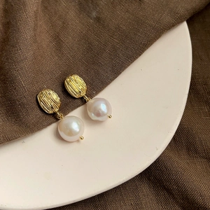 Detail of baroque pearl earrings with textured gold metal on a ceramic plate
