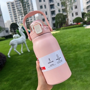 Pink stainless steel insulated water bottle with handle on a green lawn background