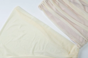 Detailed close-up of light yellow mesh fabric with delicate pleated texture and layered lace