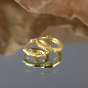 Macro shot of geometric gold hoop earrings with sharp faceted edges and mirror reflection