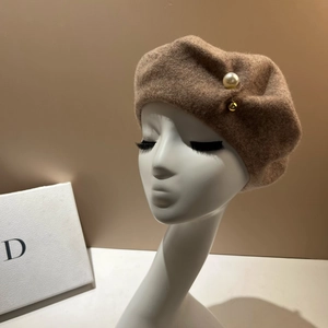 Detail of wool beret with oversized pearl and gold bead accent on camel fabric