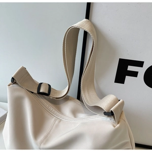 Close-up of wide nylon shoulder strap and black adjustable buckle on off-white tote bag