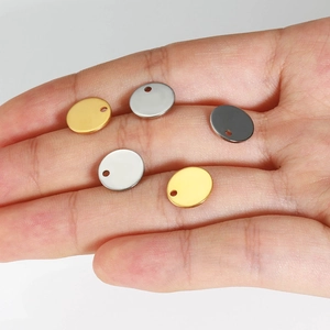 Hand holding small round 18K gold and silver stainless steel pendants for DIY jewelry