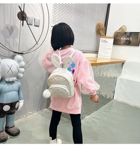 Detail of white sequin backpack with rabbit ears and plush ball on a child model