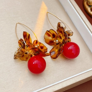 Detail view of leopard print flower earrings with golden hooks and vibrant red bead charms