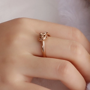 Close-up of an 18K gold plated knot ring on finger with soft texture background