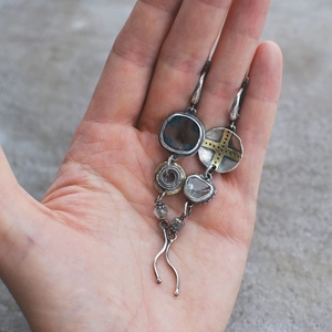Close-up of bohemian asymmetric drop earrings with cross charms and blue stones