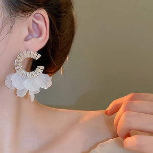 Close-up of C-shaped gold hoop earrings with white petals and sparkling zircons