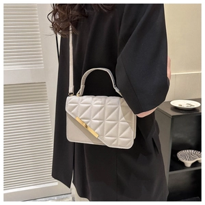 Detail of white quilted crossbody bag with golden metal trim and sleek shoulder strap