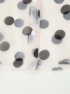 Close-up of black polka dots on beige sheer organza fabric with white button detail