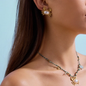 Dettaglio di orecchini a granchio dorati con perle e collana con conchiglia intrecciata blu
