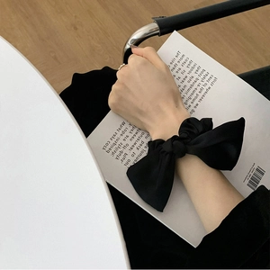 Close-up of a black satin bow scrunchie worn on a woman's wrist in a lifestyle setting